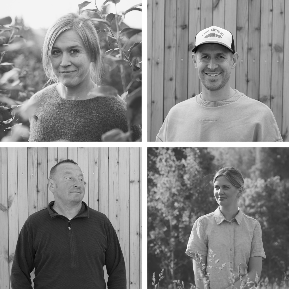 Fire mennesker som smiler i et landskap med trær og en trevegg, i svart-hvitt bilde.